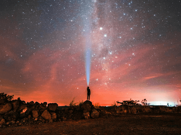 A person stands on a rock, illuminated by a bright light above, symbolizing the journey to discovering their life purpose through astrology.