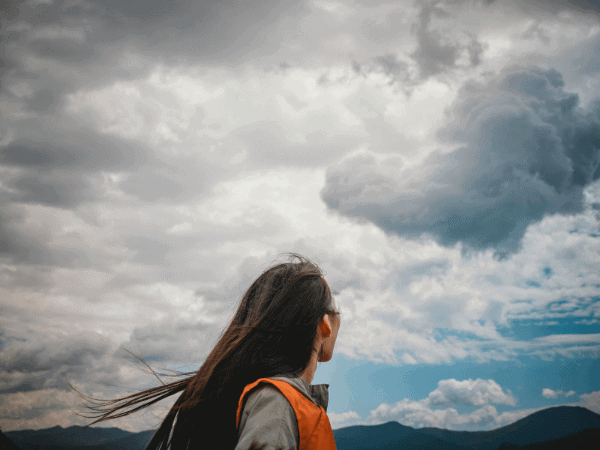 A person with long hair looking up at the cloudy sky with mountains in the background, embodying the theme of "starting over in your 30s." The scene captures a reflective moment, symbolizing the contemplation and search for clarity that often accompanies life transitions in your 30s.