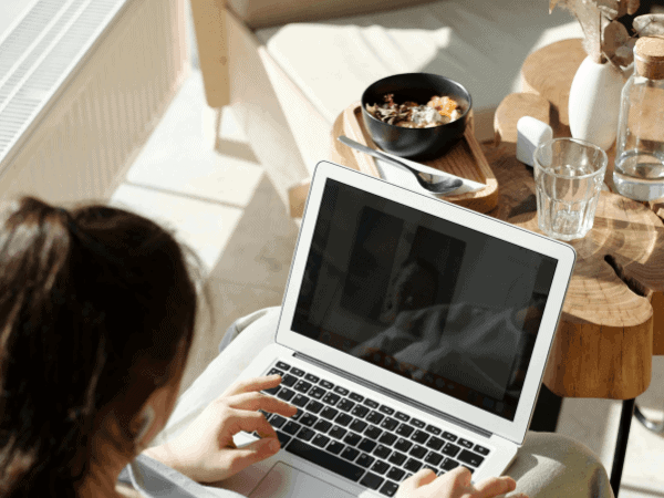 A person working on a laptop at a cozy, well-lit workspace with a bowl of breakfast on the table. The scene captures a productive moment of "starting over in your 30s," conveying a sense of comfort, focus, and the determination to rebuild or reshape one's life.