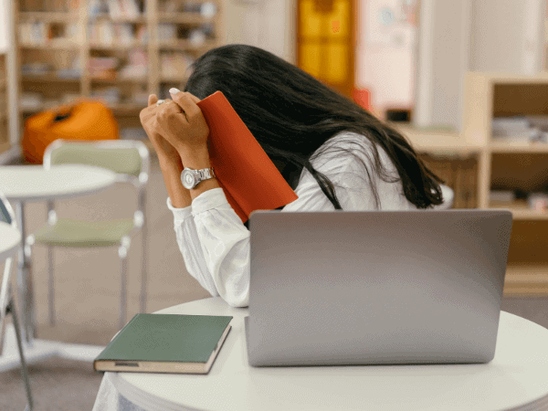 A woman sits at a table with her laptop and head in a book, reflecting on the challenges of her first business failure.