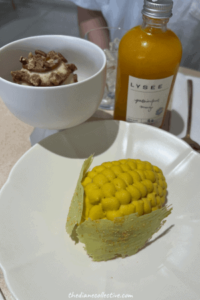 A plate featuring a corn dessert, pecan ice cream, and a bottle of passionfruit mango juice at Lysee, a French-Korean dessert restaurant located in Midtown, New York.