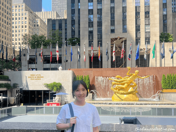 A woman stands by a fountain in front of a building at Midtown tourist attraction, Rockefeller Center.