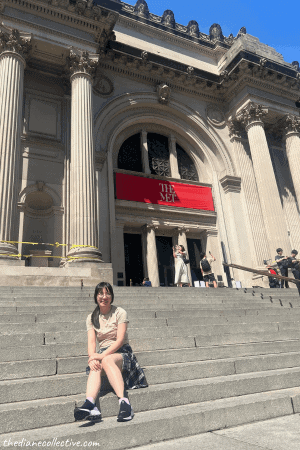 An Asian woman sits on the steps of the Metropolitan Museum of Art building in New York City.