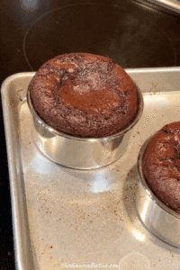 Three mini chocolate cakes on a baking pan that are fresh out of the oven with shiny tops